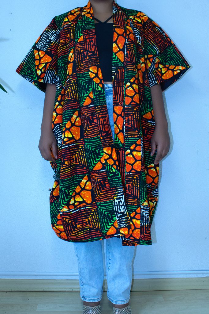 Offen getragene Bubu-Jacke mit orange-grünem Mosaikmuster über schwarzem Top und Jeans