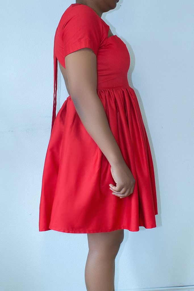 Rotes Kleid von der Seite, das Bindeband des Rückenausschnitts fällt bis zum Saum
